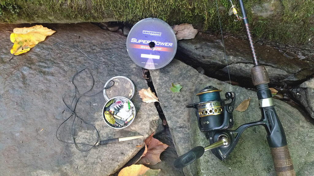 The best fishing line for trout pictured on a rock with a rod, reel, lures and a stringer.