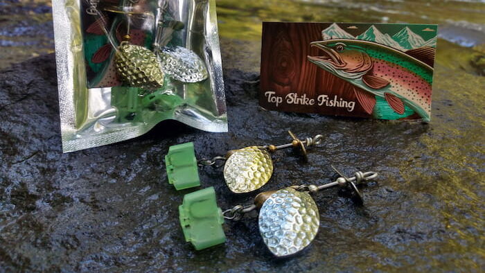 Inline fishing spinners on rock with packaging and business card. Creek in background.
