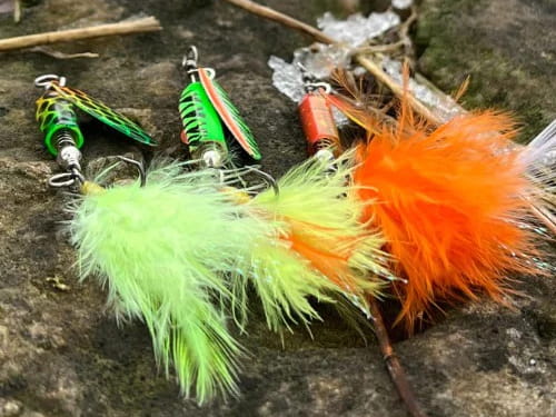 Acme Tackle Company's Rattlin Spinmaster inline spinner in several colors, photographed on a rock.