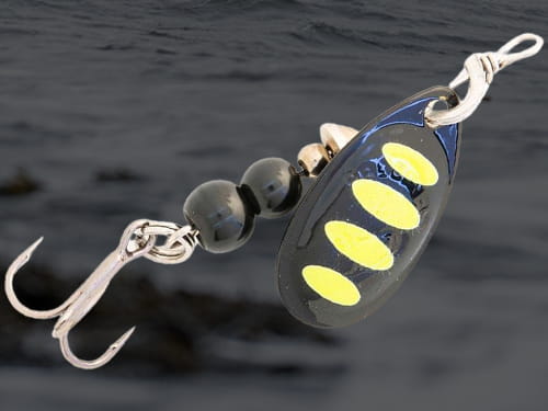 Savage Gear Rotex inline spinner in black and yellow with lake water in the background.