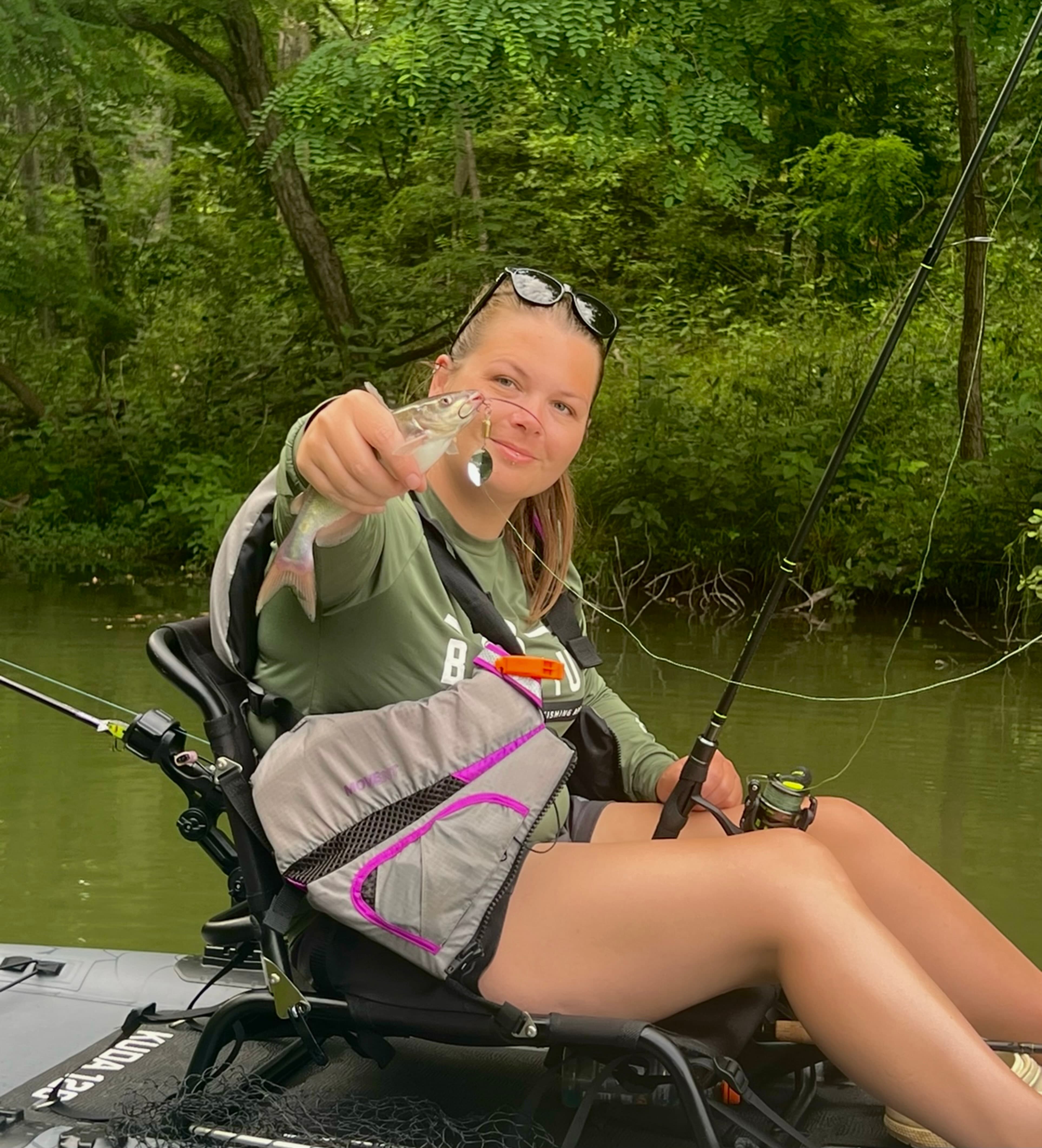 Maddie of Kast Queens holding a small catfish while sitting on a kayak.