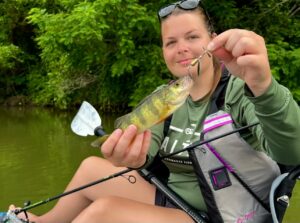 Maddie of Kast Queens holding a yellow perch while sitting on a kayak.