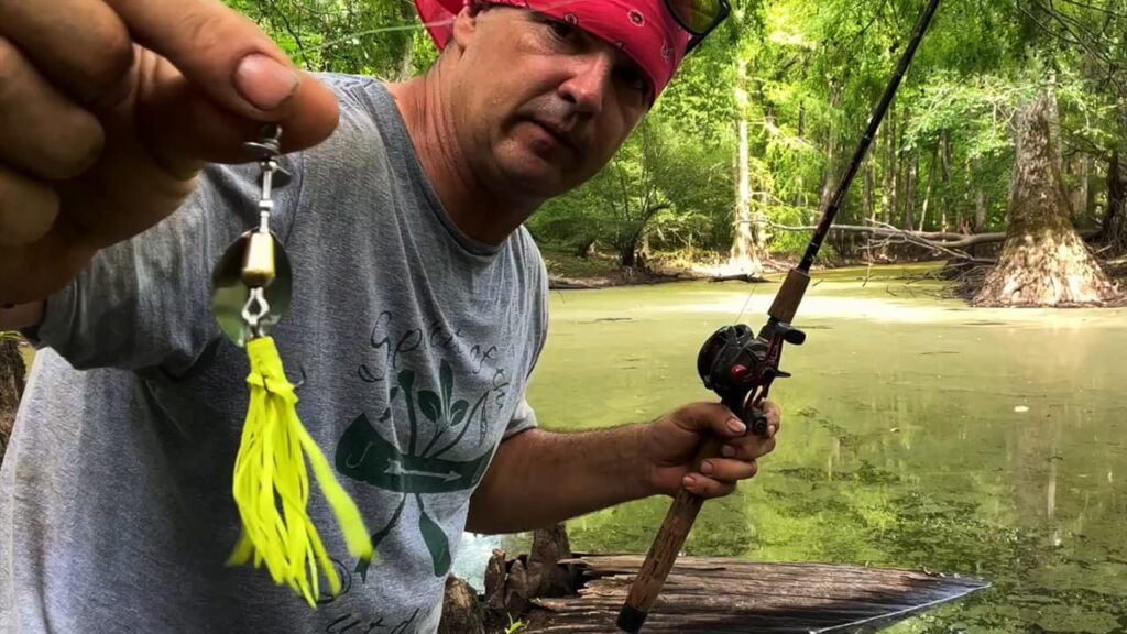 Justin of Spirit of the Outdoors holds a Top Strike Fishing spinner up to the camera with a bright yellow skirt on the hook.