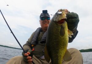 Mike of FisherMN holds a largemouth bass by the lip from his kayak on a lake in Grand Rapids, Minnesota.