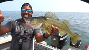 KeepFishingWithTJ holds a 25-inch Lake Erie walleye up to a camera in the rear of his boat with a view of the lake in the background.