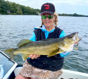 Barbara Labignan holds a gold-patterned walleye close to the camera with a Top Strike Fishing spinner in its mouth.