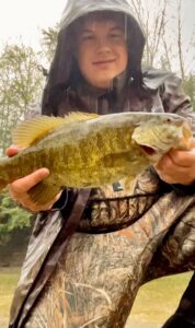 Ethan Nelson (Enelly Fishing) holds a smallmouth close to the camera on a rainy day.