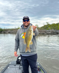 Rob Caston holds a smallmouth bass out the camera by the lip.